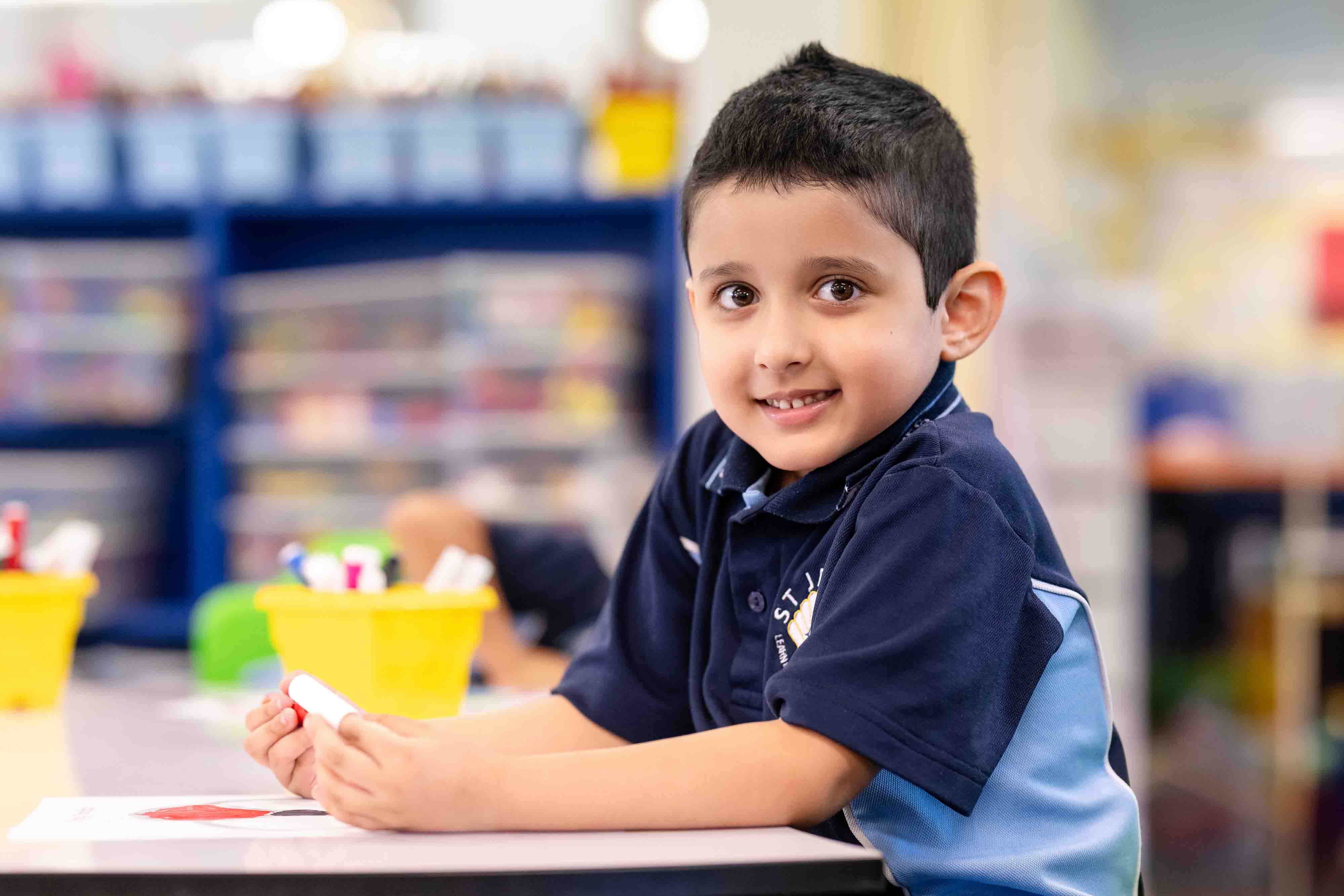 A student sitting at a desk looking at the camera. He is holding a marker and has a piece of paper in front of him.