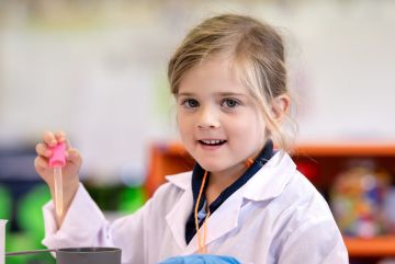 Young student wearing a lab coat uses a dropper to add liquid into a container during a classroom science activity.