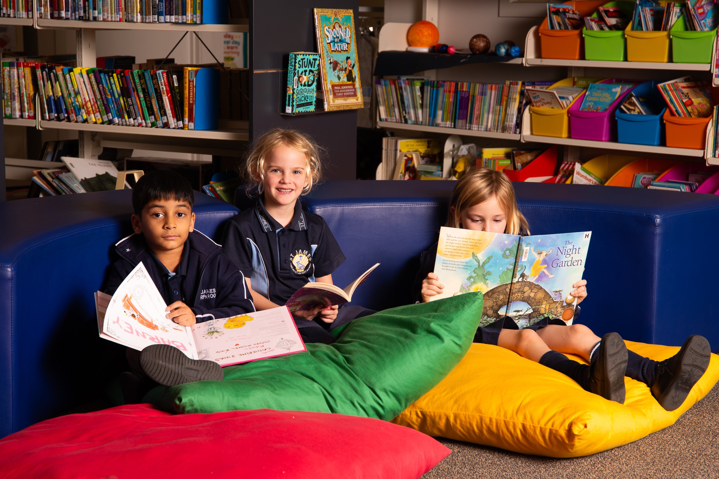 Three students sitting on cushions and reading in the library.